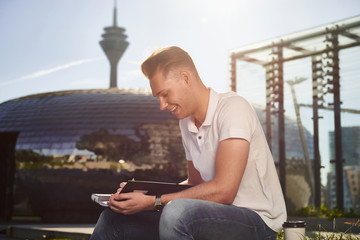 Young businessman sitting in the city outside in the sun and working 