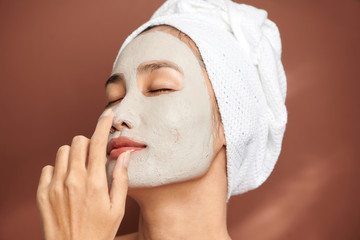 Wall Mural - Close up shot of beautiful Asian woman applies purifying mask on face, has beauty treatments