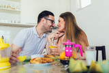 Fototapeta Panele - Young happy couple sitting in modern apartment and having breakfast together.