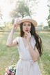 © Marina - Portrait of a young woman in a hat. Beautiful stylish girl in a summer dress, a hat and a flower in her hand.