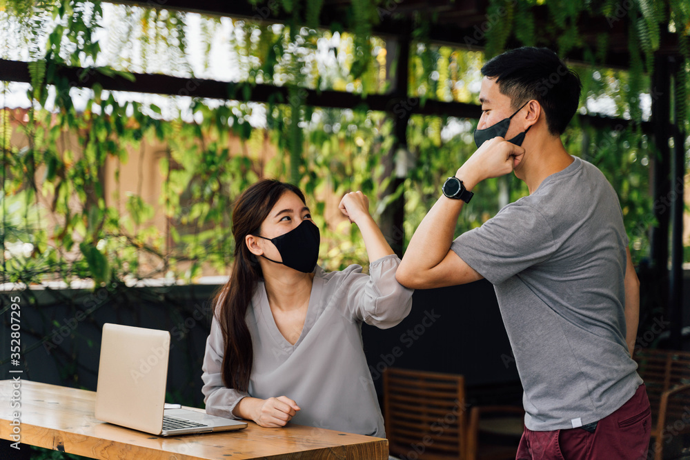 Asian woman and man friends wearing face mask outdoors. Friends greeting and shaking with elbows as new normal. Corona Virus - Covid 19 elbow bumps greeting style to prevent contact and virus spread. - obrazy, fototapety, plakaty 