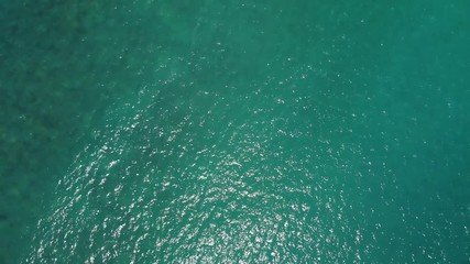 Wall Mural - Top down view from drone of green sea water and sunshine. Drone move from deep sea to sandy beach. Concept for water and sea surface.