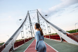 Fototapeta Tematy - Healthy active lifestyle. Pretty athlete girl in trendy sports wear with a headphones on the city bridge in a sunset light