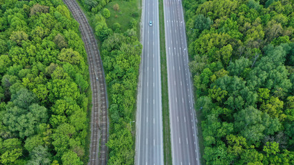 Wall Mural - Aerial view of a highway through a bright green forest. Straight road through the forest