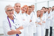© ASDF - senior female doctor standing in front of her colleagues.