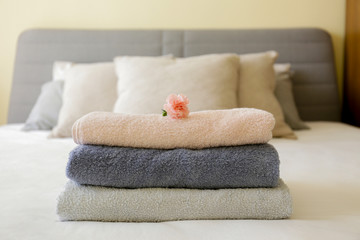 Wall Mural - Hotel room with freshly made bed, perfectly clean and ironed sheets, stack of new folded towels and single flower as decoration in natural sun light. Close up, copy space for text.