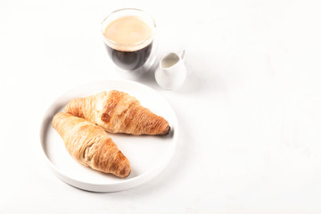 Two croissants on a plate next to a cup of coffee on light gray background with copy space.