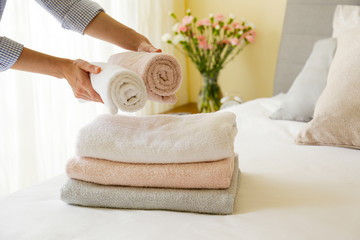 Wall Mural - House keeping lady changing the set of folded and stacked towels in hotel room with freshly made bed, perfectly clean and ironed sheets in natural sun light. Close up, copy space for text.