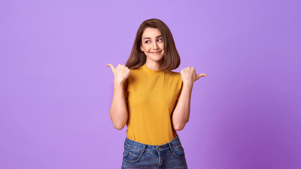 Wall Mural - Happy young woman her pointing hand over purple banner background with copy space.