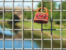 A Red Padlocked With Engraved Heart Locked To A Bridge Over Looking A River