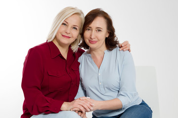 Wall Mural - Happy menopause concept. Two healthy and beautiful middle aged women isolated on white background. Woman support woman. Closeup faces and skincare makeup.