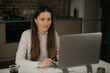 © Roman Tyukin - Remote work. A caucasian brunette woman with headphones working remotely on her laptop. A girl in a white shirt doing a video call to her business partners at her home workplace..