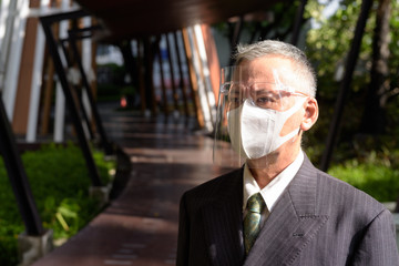 Poster - Mature Japanese businessman with mask and face shield thinking outdoors