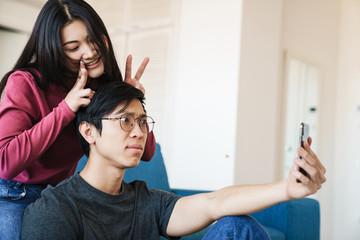 Wall Mural - Photo of asian couple making horns and taking selfie on cellphone