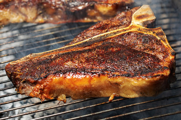 Selection of meat and vegetables grilling on a portable summer barbecue outdoors with focus to a succulent lean t-bone steak with rosemary seasoning in the foreground.