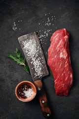 Wall Mural - Raw beef tenderloin or bavet steak with meat cleaver, salt and pepper on a dark stone background