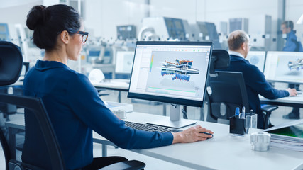 Industrial female Engineer Working on a Personal Computer, Screen Shows CAD Software with 3D Prototype of Engine. Busy Factory with Professional Workers High-Tech Machinery