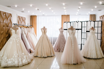 Wall Mural - Beautiful wedding dresses, bridal dress hanging on hangers and mannequins in studio, shop. Fashion look. Interior of bridal salon. Wedding show room trendy, modern.