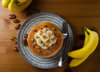 Healthy homemade sliced banana pieces and nut pancakes with bunch of whole bananas and scattered nuts on a rustic wooden background- great family meal or brunch, easy and fun to make.