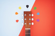 Colorful picks around acoustic guitars headstock. Flat lay on light blue and red background