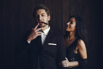 Wall Mural - Elegant man in a black suit. Couple at home. Hot woman in a black underwear. Male with cigar