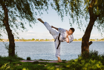 A man karate fighter in white kimono training outdoor in the park