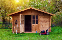 Hovel After Work In Evening, Golden Hour. Garden Shed (front View) With Hoe, String Trimmer,  Rake And Grass-cutter. Gardening Tools Shed. Garden House On Lawn In The Sunset. Wooden Tool-shed.
