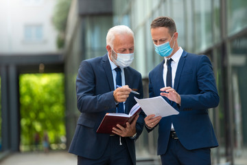 Young business man and senior business man with masks discussing something