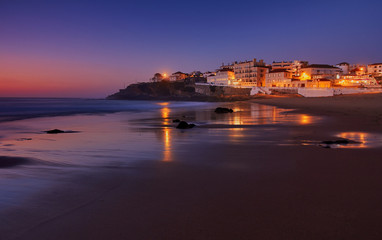 Wall Mural - Amazing landscape of the Atlantic ocean coast at dusk. Night view on the village in lights, reflecting on a sandy beach. Long exposure image. Beach of Praia das Macas. Sintra. Portugal.
