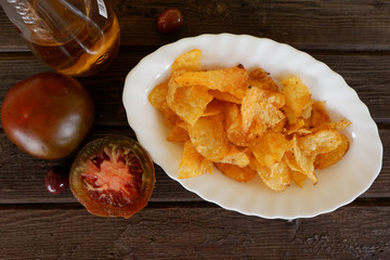 Top view of potato crisps, tomatoes and olive oil on wooden background