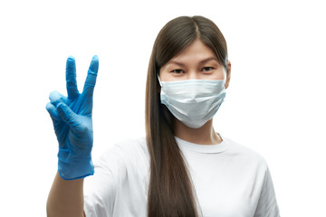 Young asian girl in medical mask and blue gloves showing victory sign on white background isolated