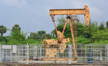 Old Rusty Oil Pump Jack Extracting Crude Oil And Natural Gas From An Oil Well In Green Oil Field Background