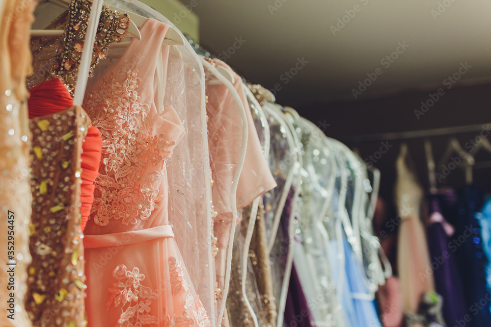 Many ladies evening gown long dresses on hanger in the dress rent shop for  the wedding day. Dresses rental concept. Wedding dress for the  wedding.selective focus.Ball gown rental concept. Stock Photo |