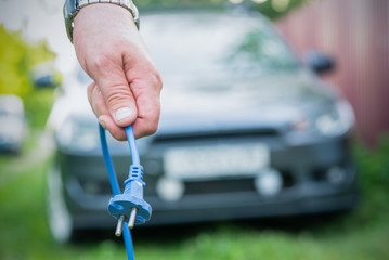 Electric car concept. Electrical plug in driver hand on car background.