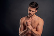 © Roman - Handsome young bearded man isolated. Cropped image of topless muscular man is standing on gray background. Man holding his wrist. Experiencing wrist pain.
