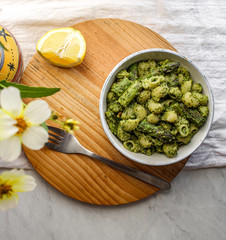 Poster - Set table with flowers and bowl of pesto pasta with asparagus and lemon. Male hand with a fork ready to eat. Top view. White background. 