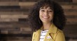 © vesperstock - MCU Young Hispanic woman in yellow leather jacket puts on 'I Voted' sticker and smiles. Wooden plank background.