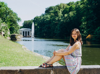 Sofia Park, Uman. Young woman sitting on a bench on the background of the lake with a fountain. The girl in a dress sits on a stone bench. Girl on a tour of the national park on a summer day.