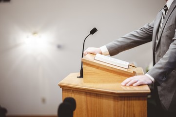 male in a formal outfit preaching the holy bible from the tribune at the altar of the church