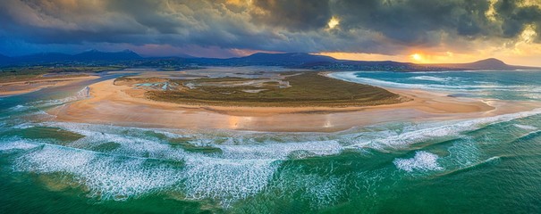 Wall Mural - panoramic aerial shot of land surrounded by the sea under an orange sky at sunset