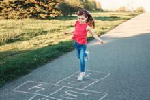 Cute Adorable Little Young Child Girl Playing Hopscotch Outdoors. Funny Activity Game For Kids On Playground Outside. Summer Backyard Street Sport For Children. Happy Childhood Lifestyle.