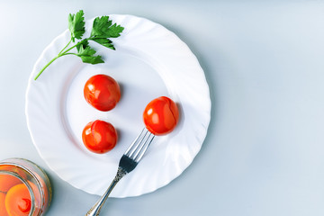 Juicy spicy marinated tomatoes with parsley on a white plate. Top view with copy space.