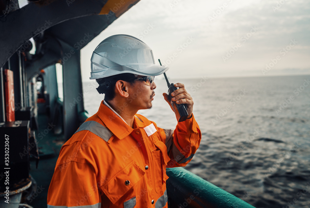 Filipino deck Officer on deck of vessel or ship , wearing PPE personal protective equipment. He speaks to VHF walkie-talkie radio in hands. Dream work at sea - obrazy, fototapety, plakaty 