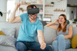 © JustLife - Smiling young man using VR headset at home on couch. Man and his wife enjoying virtual reality at her apartment.