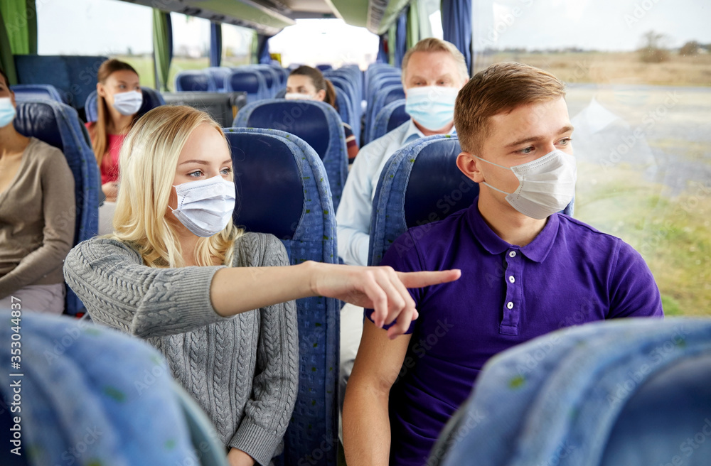 transport, tourism, road trip and people concept - young couple wearing face protective medical masks for protection from virus disease with group of tourists driving in travel bus - obrazy, fototapety, plakaty 