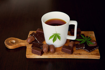 Marijuana green leaves in cup of tea on wooden background. Chocolate marijuana sweets. Delicious space candys. Copy space