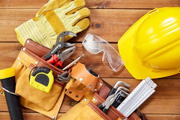 Wall Mural - repair, building and renovation concept - gloves, protective glasses, helmet and belt with different work tools in pockets on wooden boards background