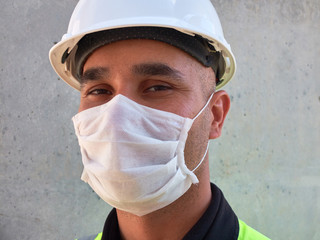 Civil engineer wears protective medical mask standing against concrete wall at construction site