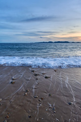 an evening view of a calm sea with rocks on a beach.