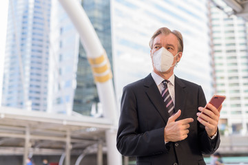 Poster - Mature businessman with mask thinking while using phone at skywalk bridge